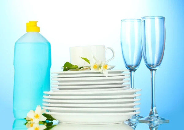Empty clean plates and glasses with dishwashing liquid on blue background — Stock Photo, Image