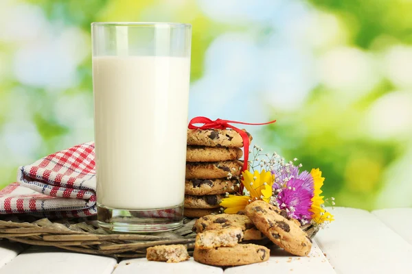 Glas melk, chocolade chips cookies met rood lint en wilde bloemen op houten tafel op groene achtergrond — Stockfoto