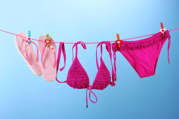 Kvinnors badkläder och flip-flops hängande på en lina på blå bakgrund — Stockfoto