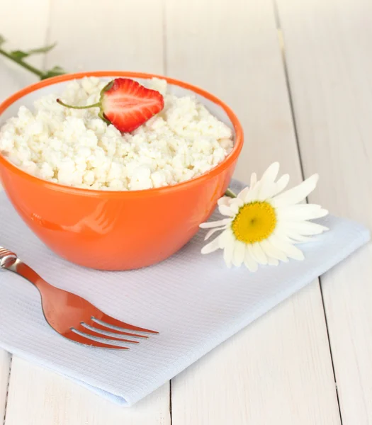 Cottage cheese with strawberry in orange bowl, fork and flower on blue napkin on white wooden table close-up — Stock Photo, Image