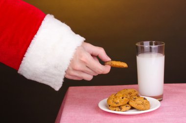 Santa Claus hand holding chocolate cookie on brown background clipart