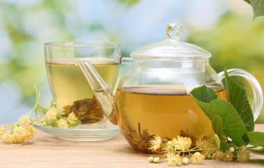 Teapot and cup with linden tea and flowers on wooden table in garden clipart