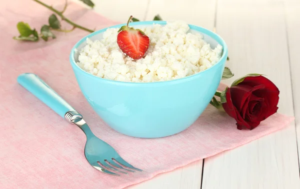 Keso med jordgubbe i blå skål, gaffel och blomma på rosa servett på vita träbord närbild — Stockfoto
