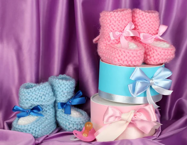 Rosa und blaue Babystiefel, Schnuller und Geschenke auf seidenem Hintergrund — Stockfoto