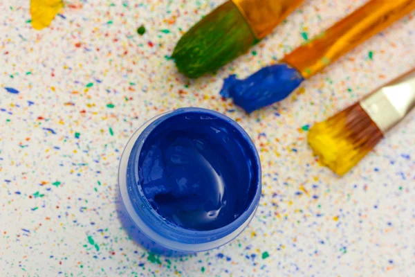 Jar com um guache azul com pincéis em salpicos coloridos fundo close-up — Fotografia de Stock