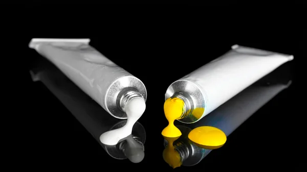 Tintas brancas e amarelas seguem dos tubos em fundo preto close-up — Fotografia de Stock