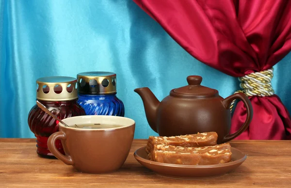 Tetera con taza y platillo con sorbete dulce sobre mesa de madera sobre fondo de cortina de cerca —  Fotos de Stock
