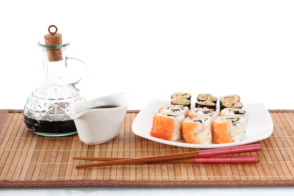 Läckra rullar serveras på vit platta med ätpinnar och sojasås på bambu matta isolerad på vit — Stockfoto