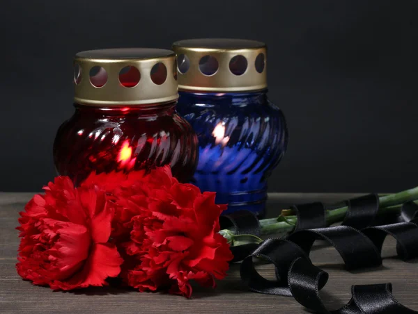 Фонарь памяти со свечами, красными гвоздиками и лентой на деревянном столе на сером фоне — стоковое фото