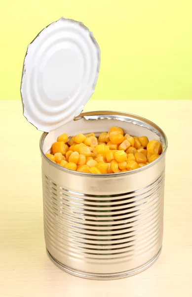 Open tin can of corn on wooden table on green background — Stock Photo, Image