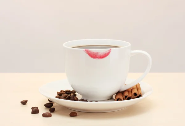 Cup of coffee with lipstick mark beans and cinnamon sticks on wooden table — Stock Photo, Image