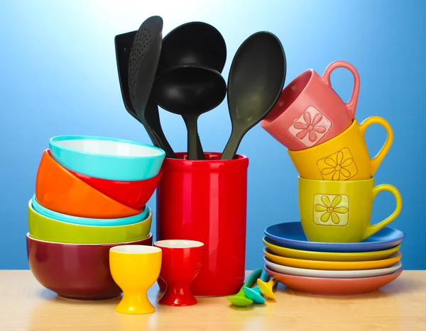 Tigelas vazias brilhantes, copos e utensílios de cozinha na mesa de madeira no fundo azul — Fotografia de Stock