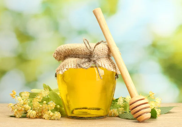 Jar with linden honey and flowers on wooden table on green background — Stock Photo, Image