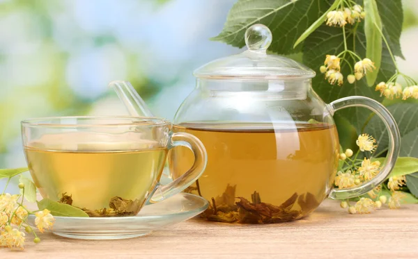 Konvice a šálek s linden čaje a květin na dřevěný stůl v zahradě — Stock fotografie