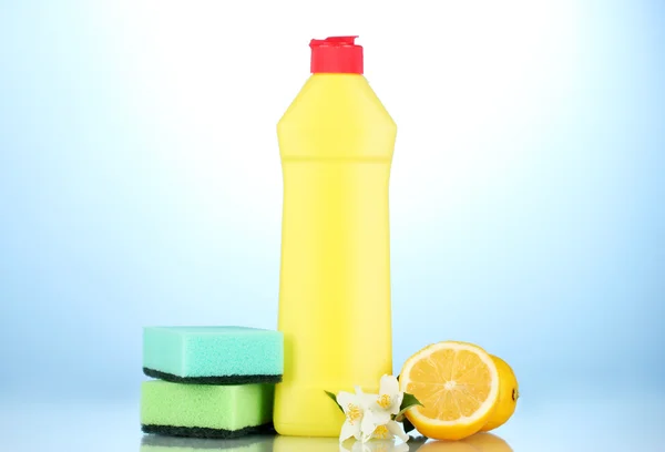 Líquido lavavajillas con esponjas y limón con flores sobre fondo azul —  Fotos de Stock
