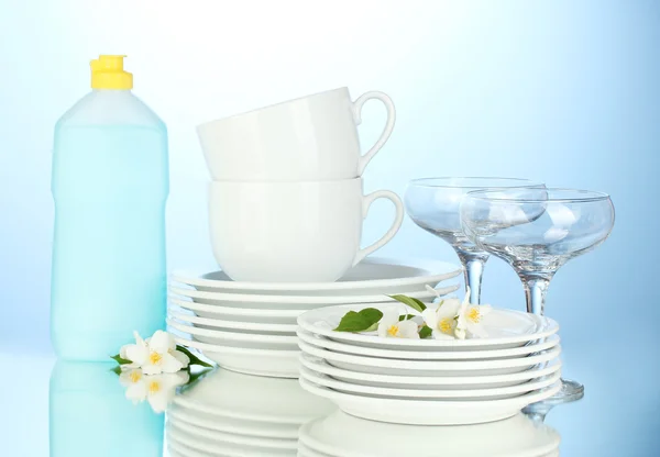 Piatti puliti vuoti, tazze e bicchieri con detersivo per piatti e spugne su fondo blu — Foto Stock