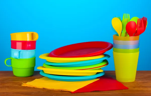 Renkli arka plan üzerinde ahşap masa üzerinde parlak plastik tek kullanımlık sofra takımları — Stok fotoğraf