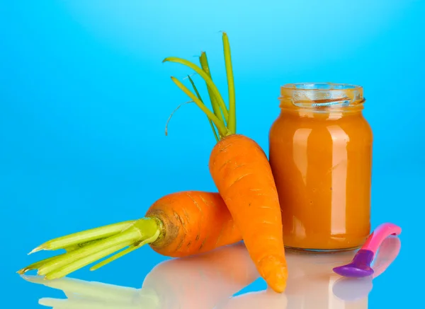 Jar with carrot baby food and spoon on colorful background — Stock Photo, Image