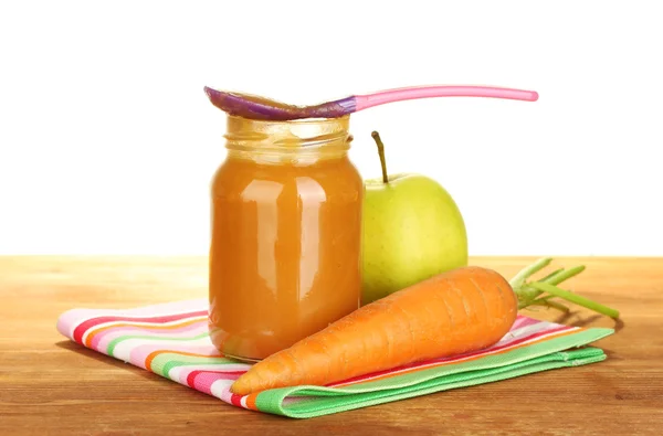 Tarro con comida para bebés de zanahoria y manzana, cuchara y zanahorias y manzanas en una servilleta colorida sobre fondo blanco de cerca —  Fotos de Stock