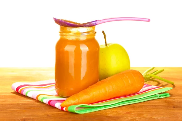 Tarro con comida para bebés de zanahoria y manzana, cuchara y zanahorias y manzanas en una servilleta colorida sobre fondo blanco de cerca —  Fotos de Stock