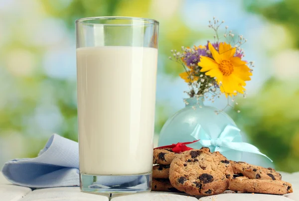 Pahar de lapte, prăjituri de ciocolată cookie-uri cu panglică roșie și flori sălbatice pe masă de lemn pe fundal verde — Fotografie, imagine de stoc