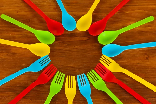 Bright plastic disposable spoons and knives on wooden table close-up — Stock Photo, Image