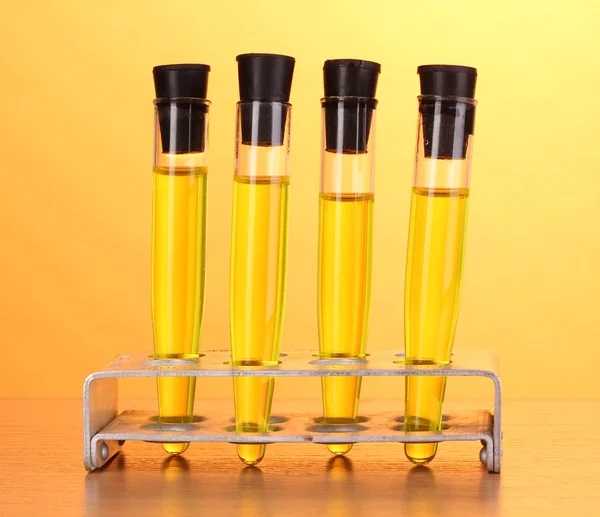 Tubes à essai avec liquide jaune sur table en bois sur fond jaune — Photo