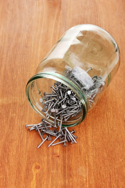 Metal nails and glass jar on wooden background — Stock Photo, Image