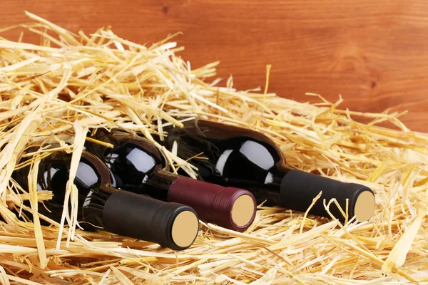 Пляшки великого вина на сіні на дерев'яному фоні — стокове фото