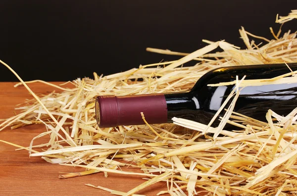 Láhev značkového vína na seno na dřevěný stůl na hnědé pozadí — Stock fotografie