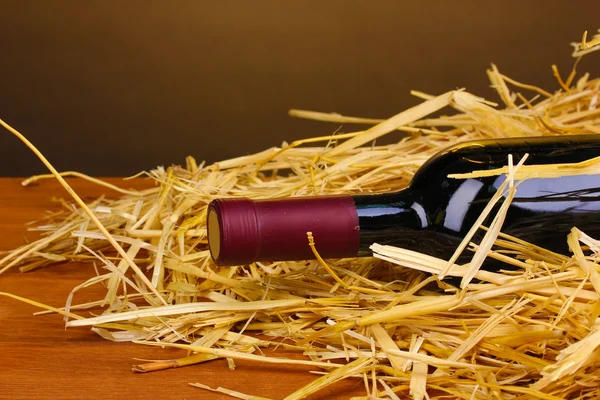 Bottle of great wine on hay on wooden table on brown background — Stock Photo, Image
