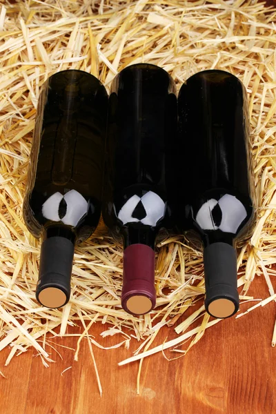Flessen van grote wijn op hooi op houten tafel — Stockfoto