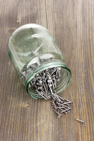 Metal nails and glass jar on wooden background — Stock Photo, Image