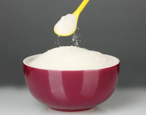 Uma tigela colorida cheia de açúcar branco com colher brilhante no fundo cinza close-up — Fotografia de Stock