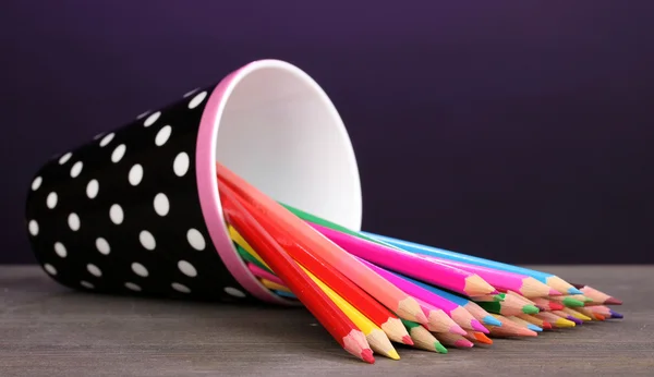 Цветные карандаши в стекле на деревянном столе на фиолетовом фоне — стоковое фото