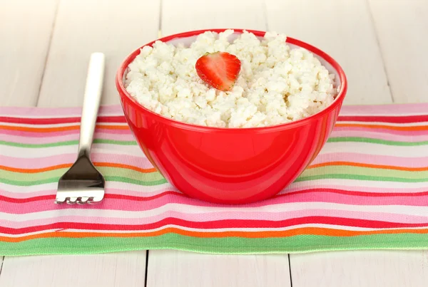 Cottage cheese with strawberry in red bowl and fork on colorful napkin on white wooden table close-up — Stock Photo, Image