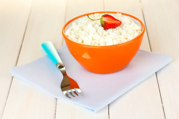 Cottage cheese with parsley in orange bowl and fork on blue napkin on white wooden table close-up