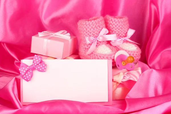 Růžové dětské boty, dudlík, pohlednice a dary na hedvábné pozadí — Stock fotografie
