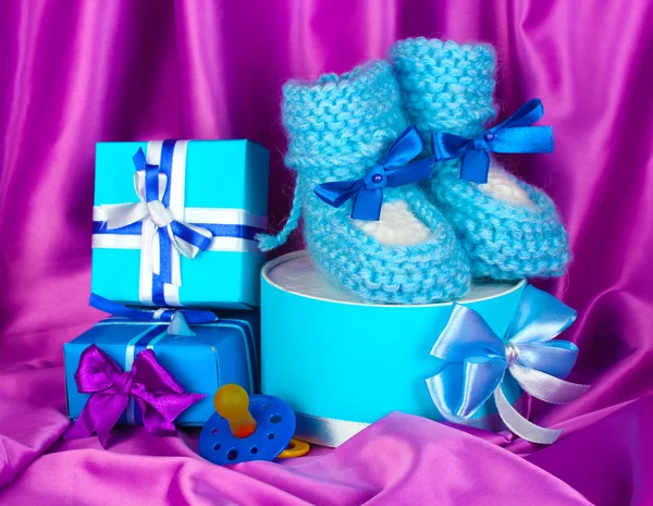 Blue baby boots, pacifier, gifts on silk background — Stok fotoğraf