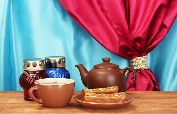 Teekanne mit Tasse und Untertasse mit süßem Serbet auf Holztisch auf einem Hintergrund aus Vorhang Nahaufnahme — Stockfoto