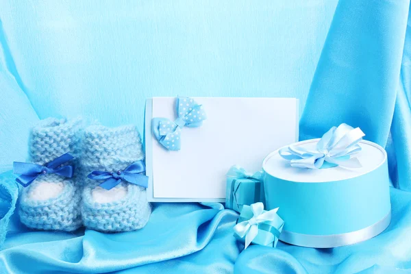 Beautiful gifts, baby's bootees, blank postcard and dummy on blue silk — Stock Photo, Image
