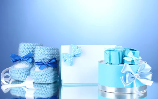 漂亮的礼物、 婴儿毛线鞋、 空白明信片和假人在蓝色背景上 — 图库照片