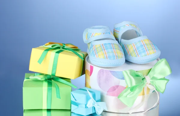 Beautiful gifts and baby's bootees on blue background — Stock Photo, Image
