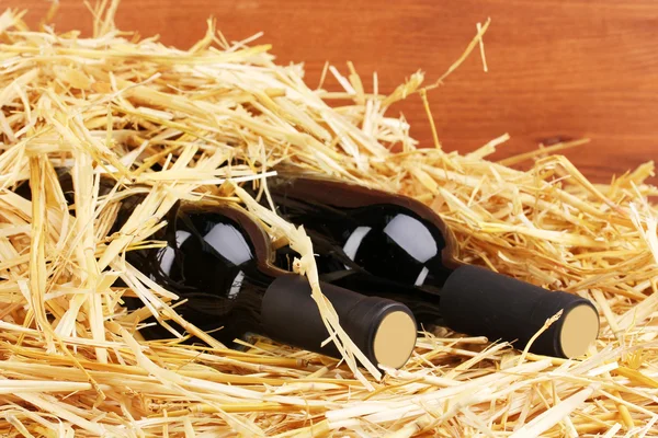 Бутылки отличного вина на сене на деревянном фоне — стоковое фото