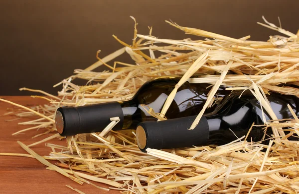 Lahví značkového vína na seno na dřevěný stůl na hnědé pozadí — Stock fotografie