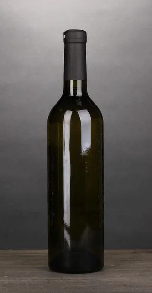 Láhev značkového vína na dřevěný stůl na šedém pozadí — Stock fotografie