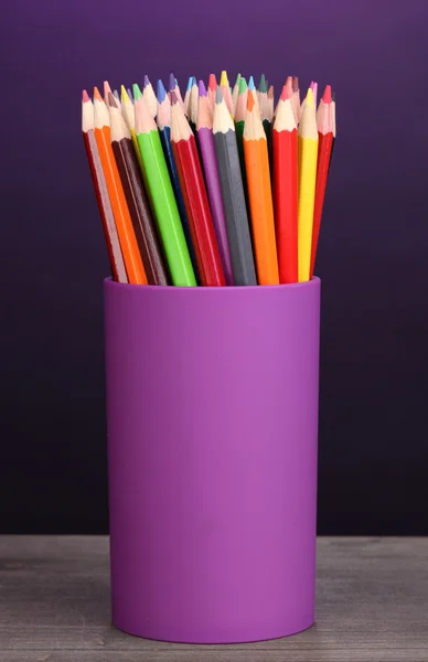 Barevné tužky ve skle na dřevěný stůl na fialové pozadí — Stock fotografie