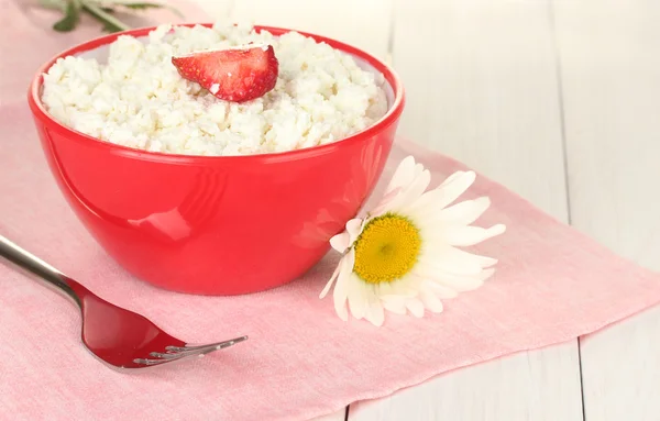 Τυρί cottage με φράουλας στην κόκκινο μπολ, πιρούνι και λουλούδι σε ροζ χαρτοπετσέτα σε λευκό ξύλινο τραπέζι κοντινό πλάνο — Φωτογραφία Αρχείου