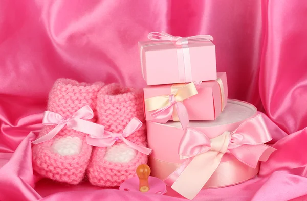 Botas de bebê rosa, chupeta, presentes no fundo de seda — Fotografia de Stock