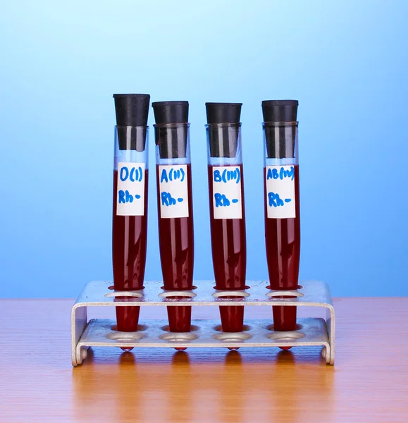 Tubos de ensayo con sangre sobre mesa de madera sobre fondo azul —  Fotos de Stock